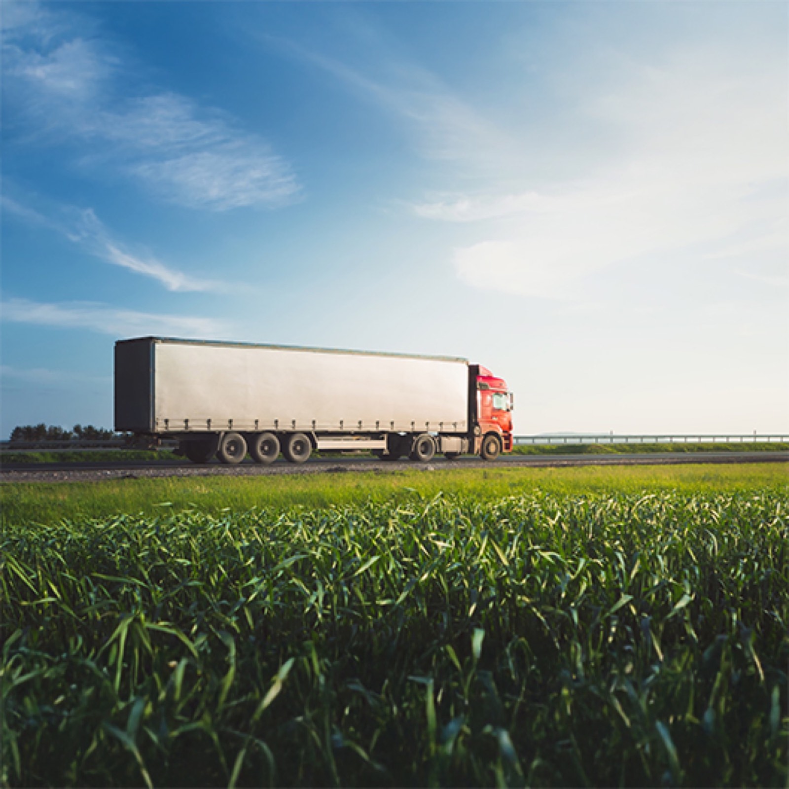 Truck carrying fertilizer stock past green fields